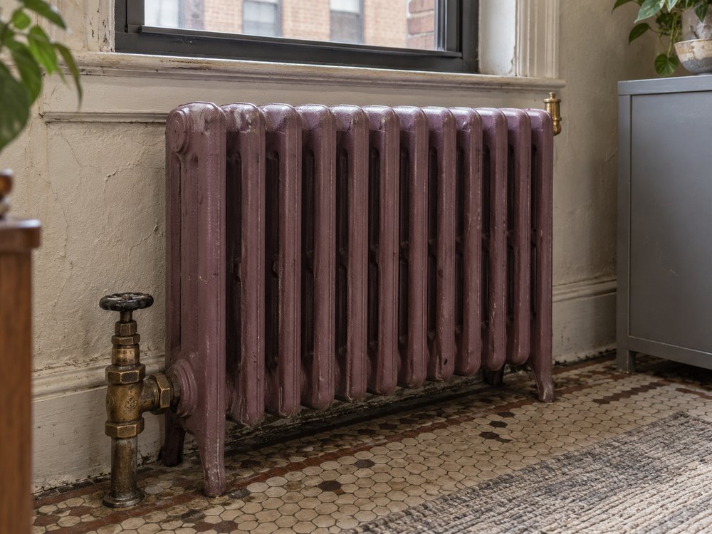 A cast-iron radiator in a pre-war Yonkers apartment with its air vent and supply valve visible.